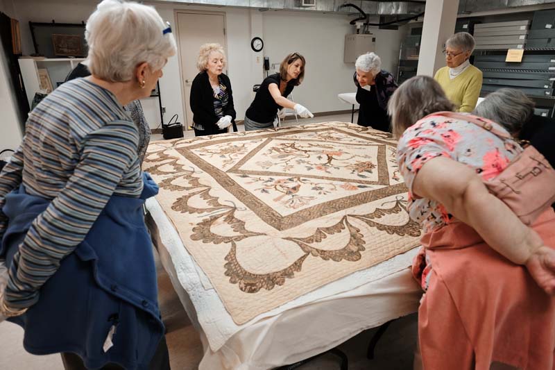 Jenny Garwood shows Trust members a quilt from MESDA’s collection.