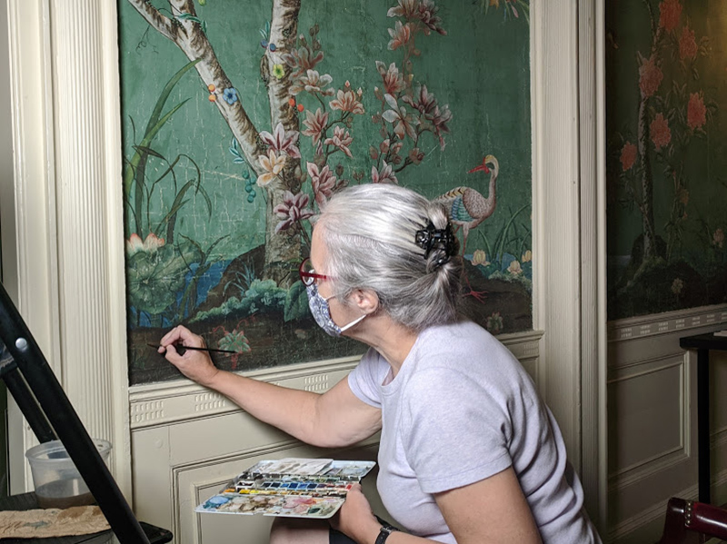 Figure 3. Conservator Lorraine Bigrigg inpaints the Chinese export wallpaper installed in the front hall at Long Hill.