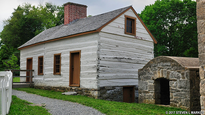 Log Structure & Ash House – The log structure as it now survives is composed of two smaller buildings (possibly slave quarters) that were joined together. By the early 20th century, it was clad in board-and-batten siding when fixed up to be the residence of an estate employee. The small stone structure next to it was used to store ashes utilized in making soap. Photo by Steven L. Markos.