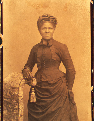 Figure 2. An elegantly dressed woman of the 1870s demonstrates the close custom fit that dressmakers of the mid- to late 19th century achieved through high-level skills that were often passed down through Black matrilines. “Studio portrait of woman wearing hat and gloves and dress with bustle,” c. 1875. Schomburg Center for Research in Black Culture, Photographs and Prints Division, The New York Public Library.