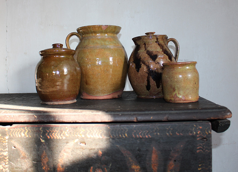 Figure 6. Four pieces of redware atop a painted dresser in the Ashley House’s South Parlor. From left: Porter Pottery, Herb jar, 1810–60, Wiscasset, ME. Redware. The Trustees of Reservations, AH.P.52; Safford Pottery, Handled pot, 1838–54, Monmouth, ME. Redware. The Trustees of Reservations, AH.P.282; Bradford Pottery, Covered pitcher, 1820–50, Kingston, MA. Redware. The Trustees of Reservations, AH.P.191; Unknown potter, Jar, 1815–40, Middlebury, VT. Redware. The Trustees of Reservations, AH.P.124. Image courtesy of The Trustees of Reservations.