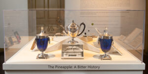 Figure 2. Installation “The Pineapple: A Bitter History” in the Orientation Gallery at Hunter House. Shown are Unknown Artist, Coffee Pot, 1791–1802, Gift of Mrs. Louise Johnston Mills, PSNC.1741.1 and Unknown Artist, Pair of Covered Baskets, c. 1820, Gift of Mrs. Alletta Morris McBean, PSNC.8337.1a-c–.2a-c. Photo courtesy of Andrea Hansen.