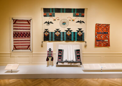 Figure 5. Installation view of a Hopi embroidered robe/manta (before 1910) attributed to an Ahbah (Hopi) craftsperson and of a contemporary Pueblo dance kilt and sash by textile artist Isabel Gonzales. The Hopi and Pueblo peoples have long established trade networks with the Navajo, which has resulted in an exchange of designs, materials, and techniques.